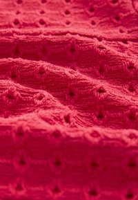 Tejido texturizado en un rosa brillante con puntos en relieve que forman un patrón de diamante, exhibiendo un material suave y esponjoso, con hilos entrelazados visibles.
