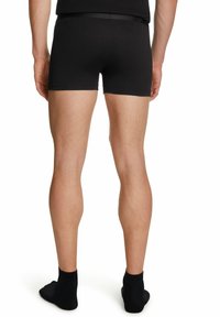 Boxer neri realizzati in tessuto elasticizzato, con una vita liscia e una vestibilità aderente. Modello mostrato da dietro con calzini neri.