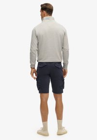 Lys grå fleecepullover med høj collar, parret med marineblå cargo shorts med sidelommer og en tekstureret finish. Beige sokker og sko.