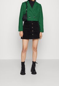 Zelený a černý károvaný krátký blazer spárovaný s černou manšestrovou sukní s předními knoflíky a kapsami a černými šněrovacími botami.