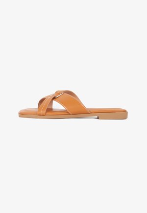 Tan faux leather slide sandals with cross-strap design, flat sole, and white stitching details. Minimalist style with a simple silver accent.
