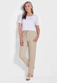 Beige joggerbroeken met een elastische tailleband en koord, voorzien van zijnaad en opgerolde boorden. Gepaard met een witte crewneck t-shirt.