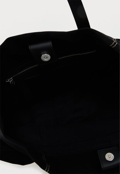 Wnętrze czarnej torby typu tote pokazujące kieszeń na zamek z uchwytem do ściągania oraz magnetyczne zapięcie na górnej krawędzi.