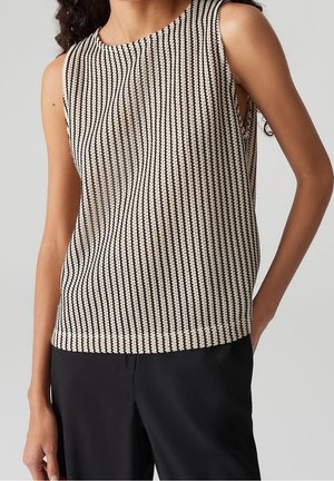 Ärmelloses schwarz-weiß gestreiftes Stricktop, getragen mit schwarzen Hosen, von den Schultern bis zur Hüfte vor einfachem Hintergrund gezeigt.