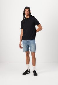 T-shirt preto de mangas curtas, calções de ganga azul-clara, sapatilhas pretas com riscas brancas e meias brancas. Design simples e casual, ajuste descontraído.