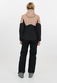 Vattentät skidjacka i svart och ljusbeige, med geometrisk design, huva och svarta byxor. Har hållbart tyg och skidstövlar.