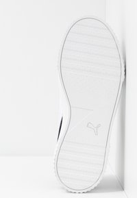 Bílá podrážka tenisky s vroubkovanou texturou, s černým akcentem poblíž strany a šedým logem Puma, nakloněná proti světlému pozadí.