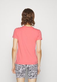 Korallrosa kortärmad t-shirt med rund halsringning, bärs med svarta och vita mönstrade shorts, visad bakifrån.