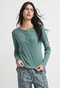 Teal lange mouw top met henley halslijn en vier knopen, met een gestructureerd patroon. Gecombineerd met gestreepte pyjamabroek in gedempte kleuren.