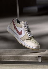 Baskets beige et crème avec une tige en cuir texturé, des accents rouges, un bout perforé et des lacets gris, dotées d'une semelle en caoutchouc.