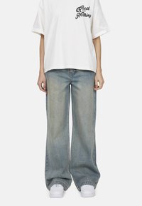 T-shirt bianca oversize con stampa nera "Good for Nothing", abbinata a jeans a gamba larga blu chiaro e sneakers bianche.