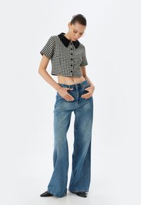 Top corto en blanco y negro con diseño de pata de gallo y cuello negro, combinado con jeans de mezclilla azul de cintura alta y corte acampanado, y zapatos negros de punta.