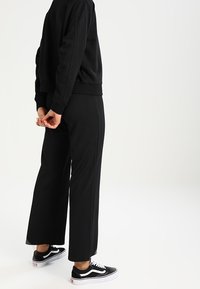 Sweat-shirt noir et pantalon à jambes larges, fabriqués dans un tissu doux. Associés à des baskets noires et blanches. Accent mis sur un design simple et une couleur unie.