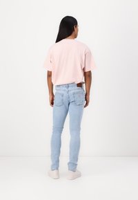 Camisa de manga corta rosa claro combinada con jeans ajustados azul claro, con un parche de cuero marrón y sutiles detalles en el bolsillo trasero.
