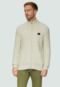 Hellbeige Reißverschluss-Pullover mit Rautenmuster, gerippten Bündchen und hohem Kragen. Verfügt über ein kleines schwarzes Logo auf der Brust.