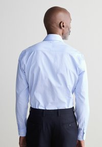 Hellblau gestreiftes Hemd mit Button-Down-Kragen, langen Ärmeln und glatter Textur, kombiniert mit dunklen Hosen.