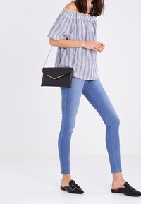 Pruhovaný top s odhalenými rameny v světle modré a bílé barvě, doplněný o úzké modré džíny a černé nazouvací boty se zlatou sponou.