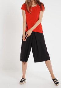 Czerwony top z krótkim rękawem połączony z czarnymi szerokimi spodniami culottes i espadrylami w biało-czarny pasek. Prosty fason z luźnym krojem.