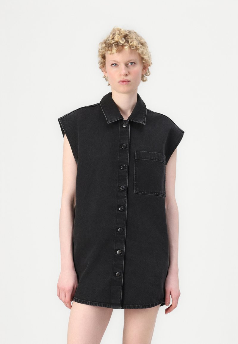 Zwarte denim jurk met korte mouwen, knoopsluiting aan de voorkant en een borstzak. De stof heeft een gladde textuur en een klassiek kraagontwerp.