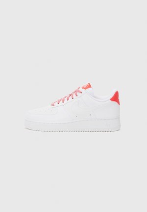 White sneaker with red accents, featuring a smooth leather upper, perforated toe for breathability, and a textured rubber sole.