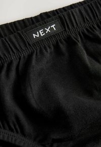 Schwarze Baumwollunterwäsche mit elastischem Bund, ausgestattet mit einem gestickten Etikett, das das Wort "NEXT" in einer weißen, handgezeichneten Schriftart zeigt.