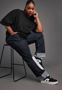 Svart oversized t-shirt i kombination med mörka denimjeans med uppvikta avslut. Sneakers i svart och vitt med platt sula. Enkelt design.