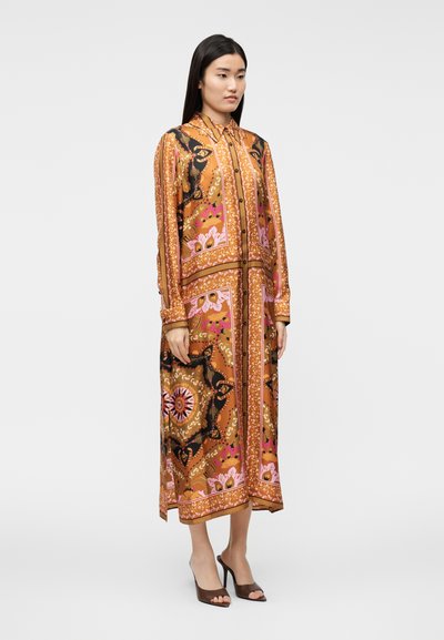 Ilga, oranžinė ir rožinė su juodais akcentais, raštuota suknelė su apykakle, sagomis ir šilkinio pojūčio audiniu, dėvima su rudos spalvos aukštakulniais sandalais.