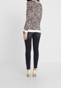 Pull imprimé léopard avec poignets blancs, associé à un jean foncé ajusté et des talons hauts beige clair. Texture lisse, coupe décontractée.