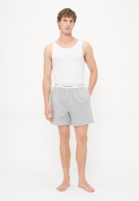 Graue Baumwollshorts mit einem elastischen Bund, versehen mit "Calvin Klein"-Markierung, kombiniert mit einem weißen ärmellosen Tanktop.