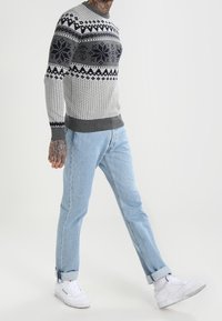 Pull en maille grise avec des motifs flocons de neige et géométriques bleu marine, assorti à un jean bleu clair aux revers roulés et des baskets blanches.