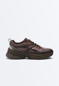 Brauner und dunkel mauvefarbener Sportschuh mit dicker Sohle, Mesh-Obermaterial, Schnürverschluss sowie verstärkten Zehen- und Fersenpartien.
