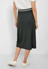 Knee-lange, mørkegrøn nederdel med elastisk talje og hvide striber. Glat tekstur, A-formet silhouette, parret med hvide sneakers.