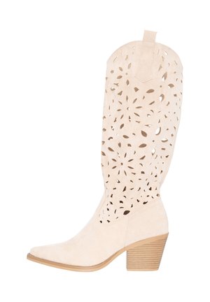 Beige suède laarzen tot halverwege de kuit met gestapelde blokhak en een ingewikkeld bloemenuitgesneden patroon op de schacht.