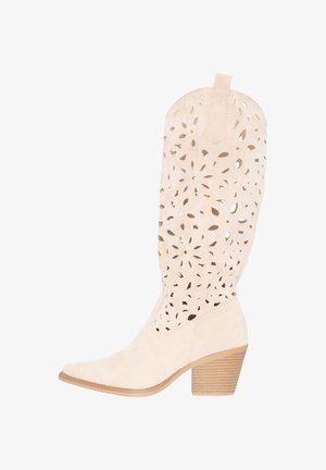 Beige suède laarzen tot halverwege de kuit met gestapelde blokhak en een ingewikkeld bloemenuitgesneden patroon op de schacht.