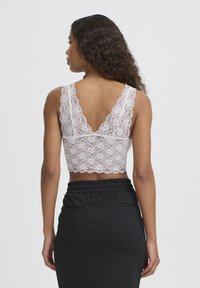 Haut court en dentelle rose clair avec bords festonnés et dos en V, associé à une jupe à taille noire avec poches latérales.