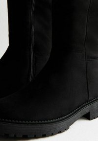 Czarne zamszowe kozaki za kolano o gładkiej fakturze, z detalami w postaci bocznego zamka błyskawicznego oraz grubą gumową podeszwą z rowkowanym wzorem.