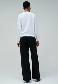 Sudadera blanca de manga larga con puños acanalados, combinada con pantalones negros de tiro alto y pernera ancha, que muestran un diseño limpio y minimalista.