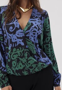 Blouse à manches longues noire avec un motif floral vert et bleu, présentant un décolleté en V profond et un tissu doux avec une coupe loose.