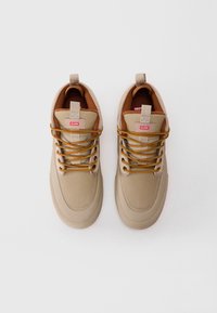 Para beżowych sneakersów marki Globe z żółtymi i brązowymi sznurówkami, wyłożonych brązowym materiałem, wyeksponowanych z widoku z góry na białym tle.