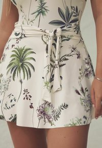 Minirock mit floralen Mustern aus leichtem Stoff; mit grünen Palm- und lila Pflanzendesigns, einem gebundenen Bund und einer glatten Textur.