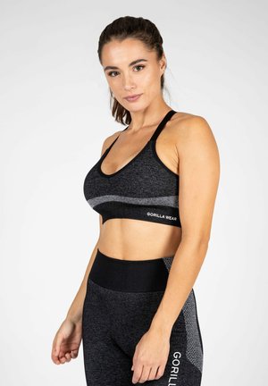 Soutien-gorge de sport noir avec accent gris, présentant un décolleté en scoop et des bretelles réglables. Le matériau est texturé et ajusté. Logo de la marque visible.