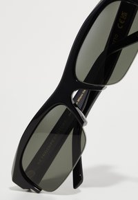 Lunettes de soleil noires surdimensionnées avec des verres foncés. Présentent une monture audacieuse et angulaire avec des accents en métal argenté. Temples texturés avec logo.