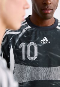 Black and white Adidas sports jersey with number 10 worn by a man, with a blurred profile of another person in the foreground.