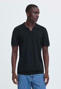 Polo noir en maille avec col en V et manches courtes, associé à un jean en denim bleu clair. Design simple et tissu texturé.