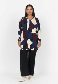 Tunique à manches longues avec un motif abstrait multicolore présentant des nuances de bleu marine, crème et bordeaux sur un tissu doux. Associée à un pantalon noir à jambes larges.