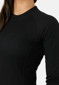 Schwarzes, eng anliegendes Langarmshirt mit gerippter Textur, rundem Halsausschnitt und seitlichen Nähten. Der Stoff hat eine glatte Oberfläche.
