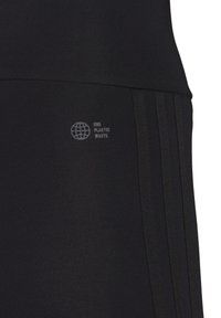 Melni legingi ar gludu, elastīgu audumu, kas aprīkoti ar trim vertikālām svītrām un mazu "Beidz plastmasas atkritumus" logo tuvu jostasvietai.