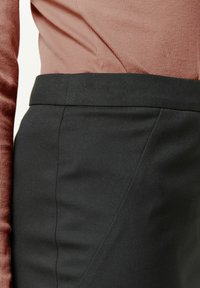 Jupe noire avec une texture lisse, dotée d'une coupe ajustée et d'une taille haute, associée à un haut rose côtelé.
