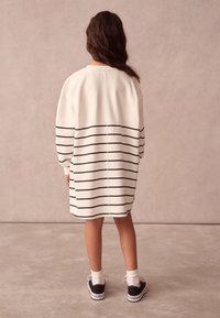 Hvid sweatshirt-kjole med navyblå horisontale striber, afslappet pasform, nedslåede skuldre og ribkanter. Stylet med sorte sneakers og hvide sokker.