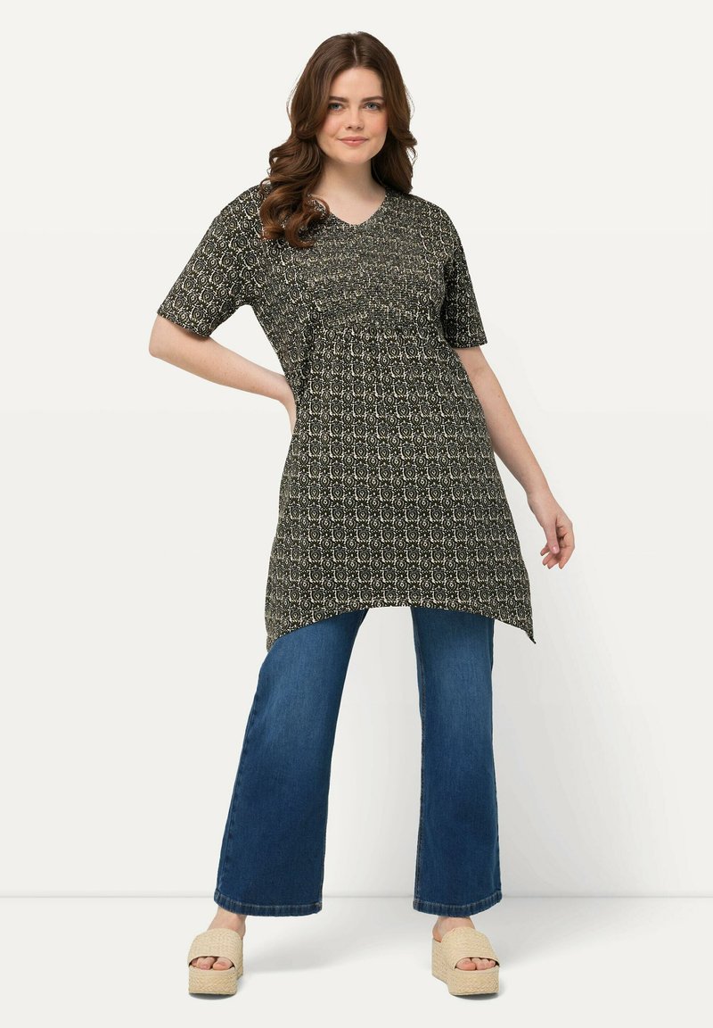 Zwart-wit gestreepte tuniek met korte mouwen, v-hals en asymmetrische zoom, gecombineerd met blauwe wijdlopende jeans en beige platform schoenen.